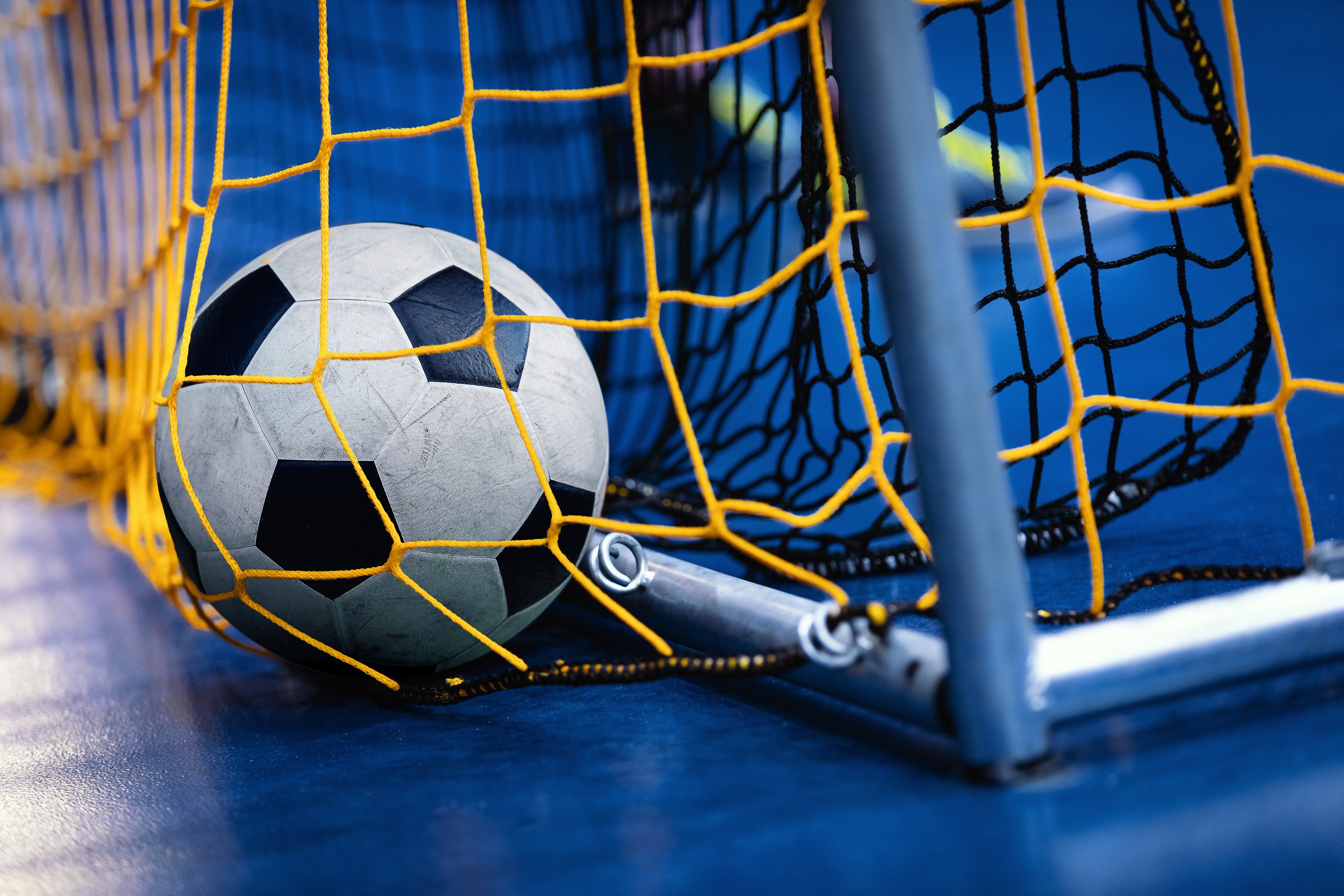 Indoor Soccer Futsal Ball on Goal with Net and Blue Background.